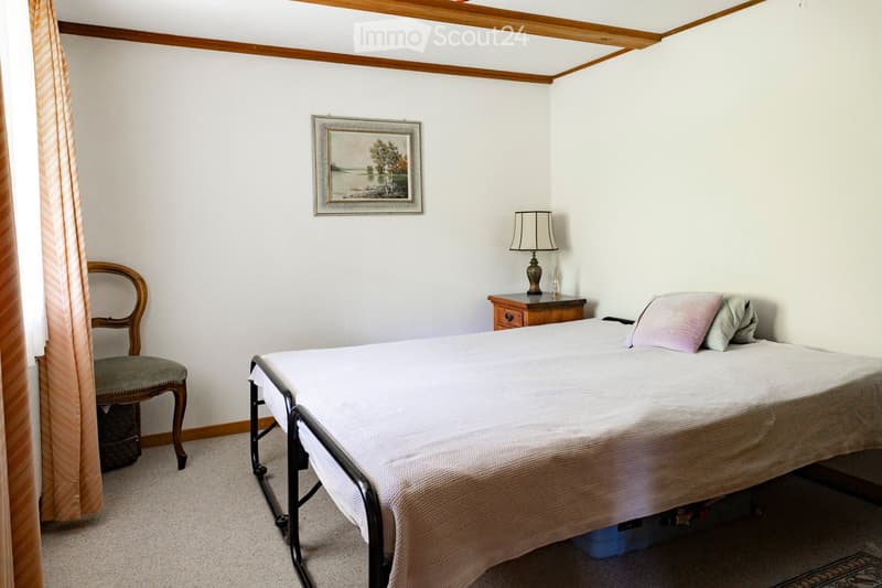 Cozy bedroom with a single bed, nightstand, chair, and a framed picture on the wall.