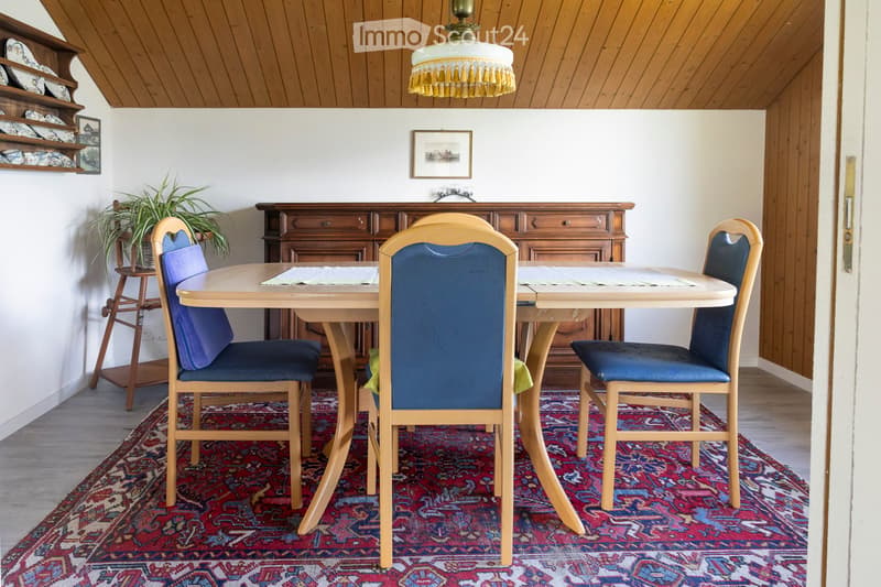 Dining room with a wooden table, four chairs with blue cushions, a wooden cabinet, a potted plant, and a chandelier.