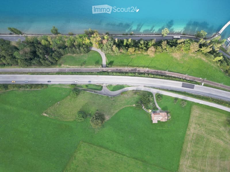 Aerial view of a rural area with a small house, green fields, roads, and a body of water in the background.