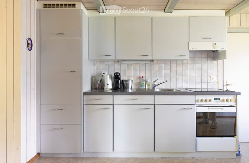 Modern kitchen with white cabinets, stainless steel sink, oven, and countertop items including a coffee maker and bottles.