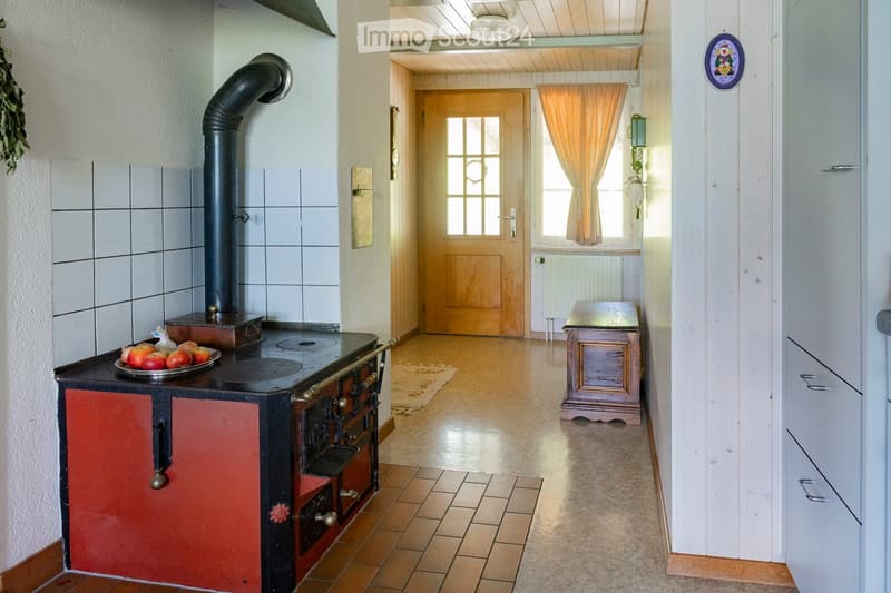 Hallway with wooden floor, white walls, a door leading to another room, a small table, and a stove with a fruit bowl on it.