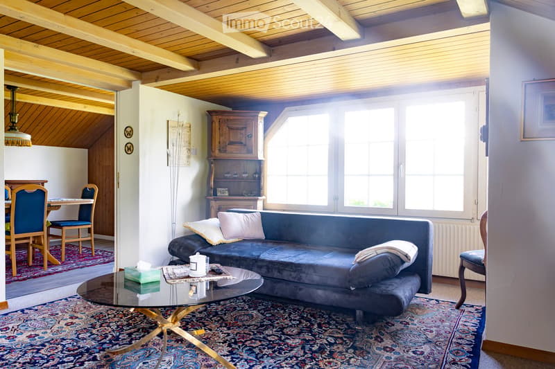Living room with a blue sofa, glass coffee table, dining area with chairs and table, wooden cabinet, and large windows letting in natural light.