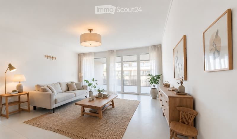 Bright living room with white walls, large windows, and sliding glass doors leading to a balcony. Features a light-colored sofa, wooden coffee table, side table, and decorative plants.