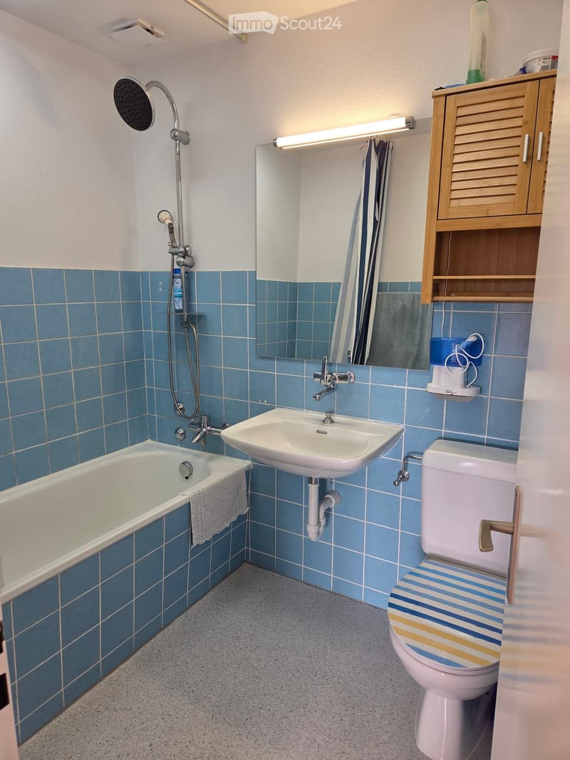 Bathroom with blue tiled walls, bathtub, sink, toilet, mirror, and a wooden cabinet.