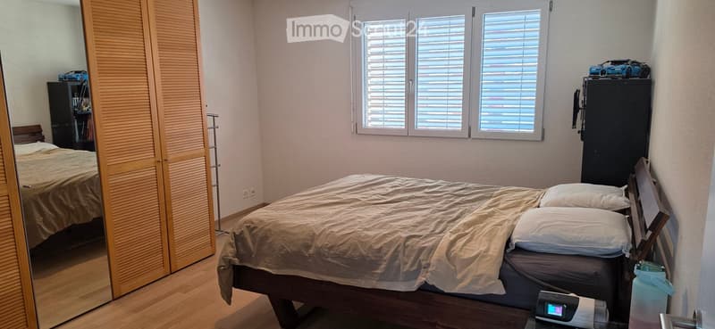 Bedroom with a large bed, mirrored wardrobe, nightstand, and a small shelf with a toy car on top.