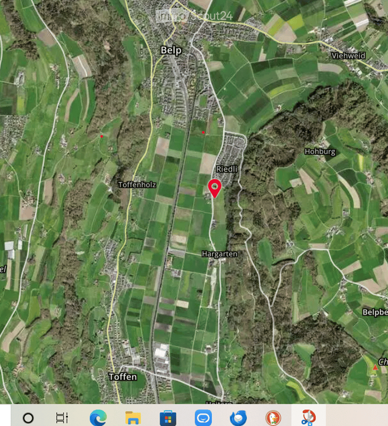 Aerial view of a rural area with fields, roads, and small clusters of buildings. The map shows various locations including Belp, Riedli, and Toffenholz.