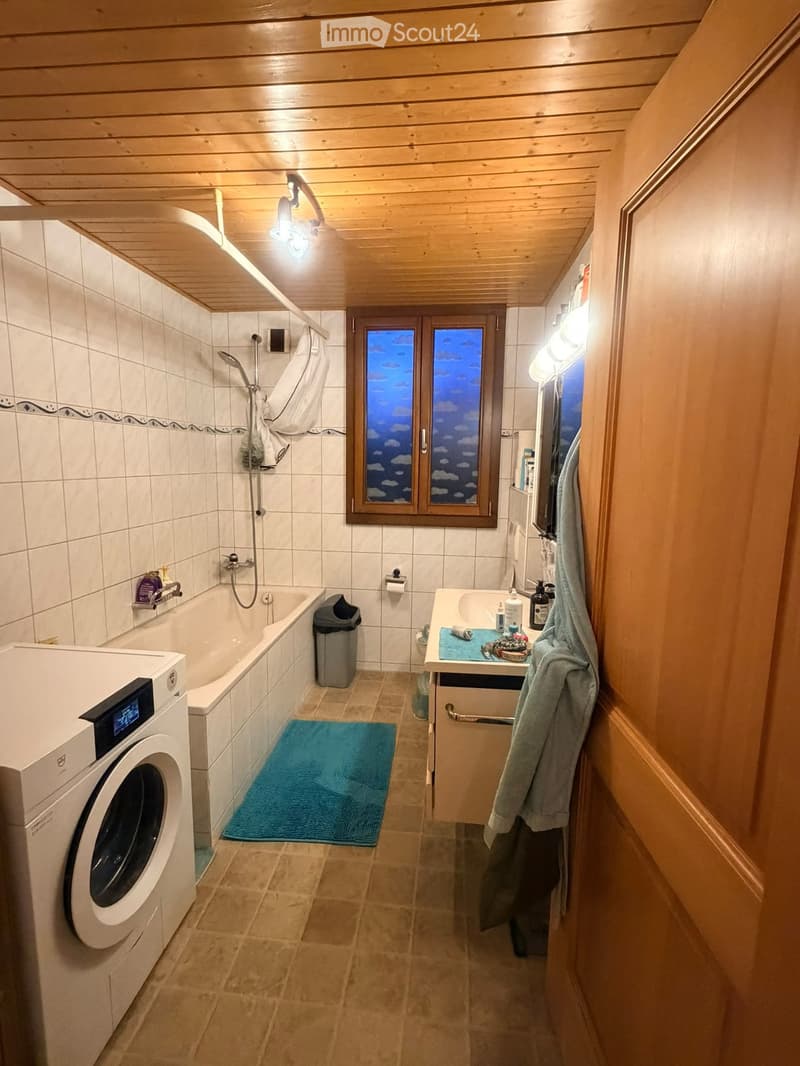 Bathroom with wooden ceiling, tiled walls, bathtub, washing machine, sink, mirror, towel, and a window with a scenic view.