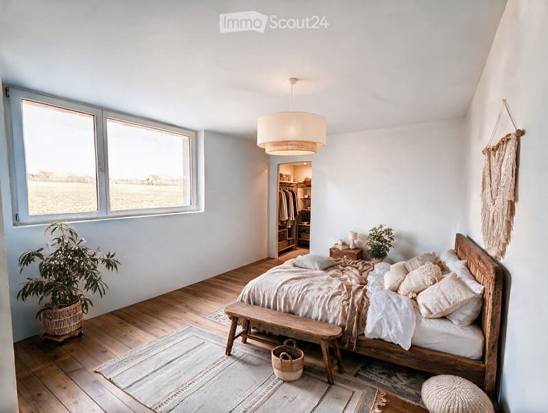 Bright bedroom with wooden floor, large windows, a wooden bed with white bedding, a bench at the foot of the bed, a hanging woven decoration, and a potted plant near the window.