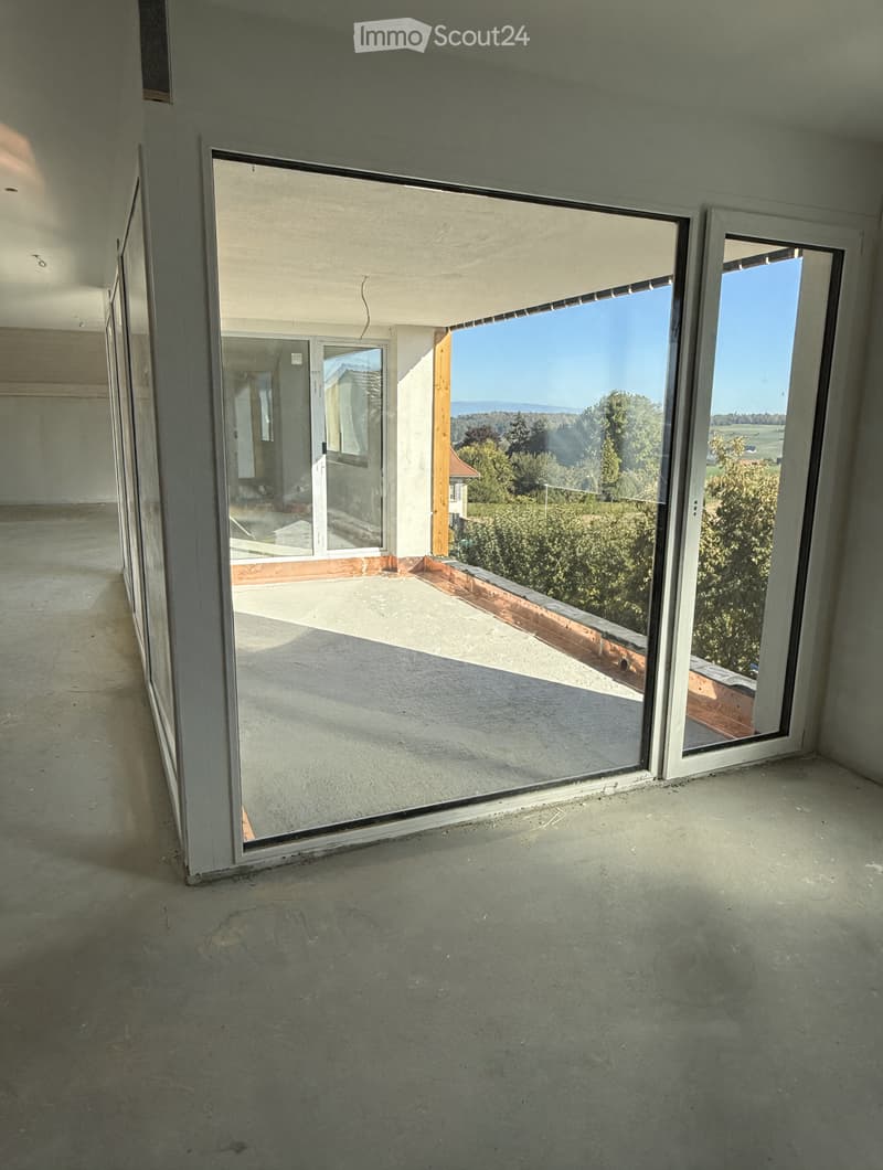 Empty room with large glass sliding doors opening to a balcony with scenic views of trees and fields.