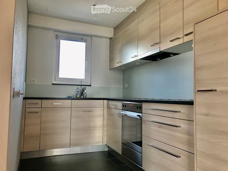 Modern kitchen with light wood cabinets, stainless steel oven, and a window above the sink.