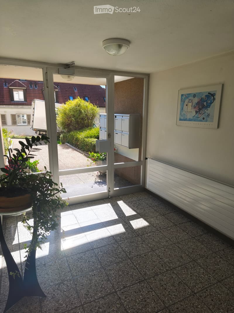 Hallway with tiled floor, large window, radiator, and a framed artwork on the wall.