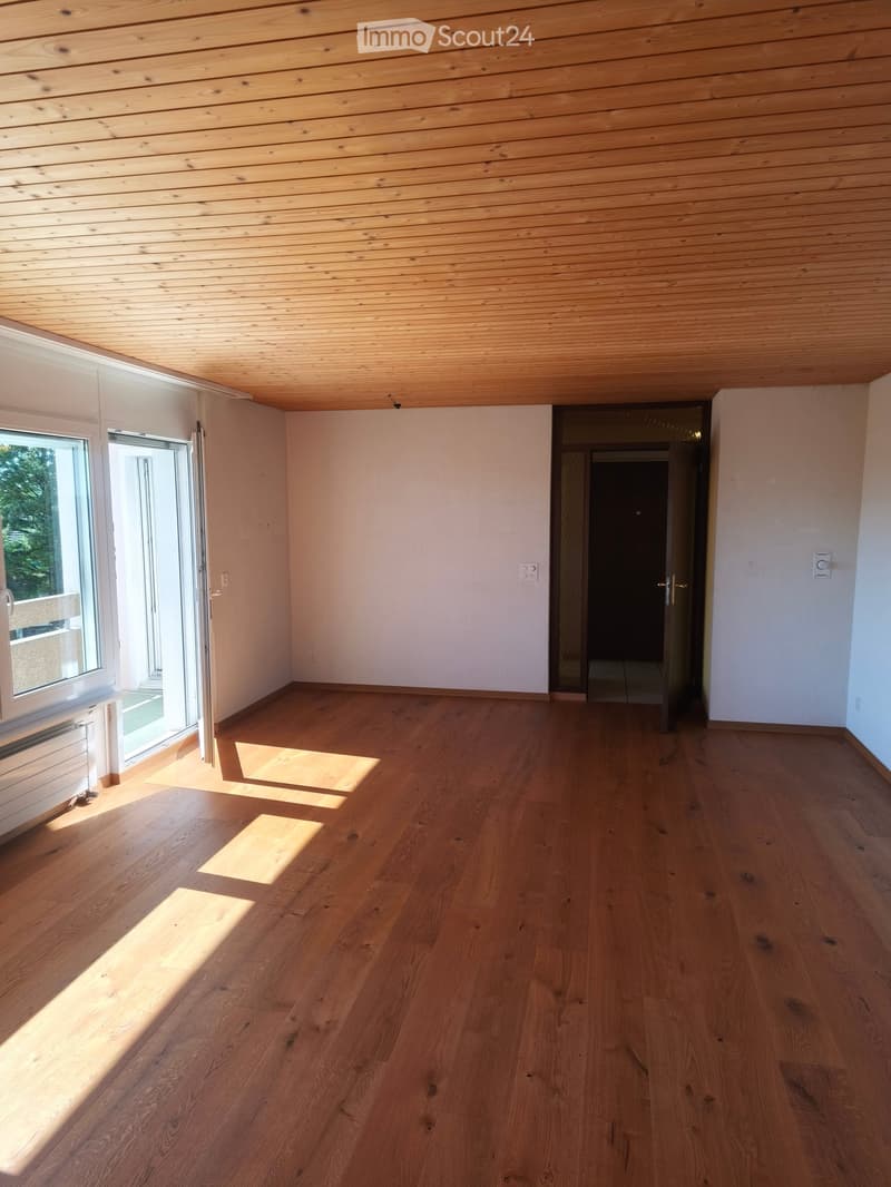 Empty room with wooden floor and wooden ceiling, large windows, and a doorway leading to another space.