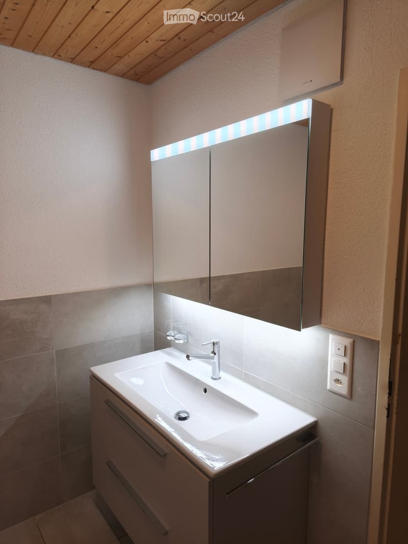 Modern bathroom with a white sink, chrome faucet, mirrored cabinet, and two small cups on the counter.