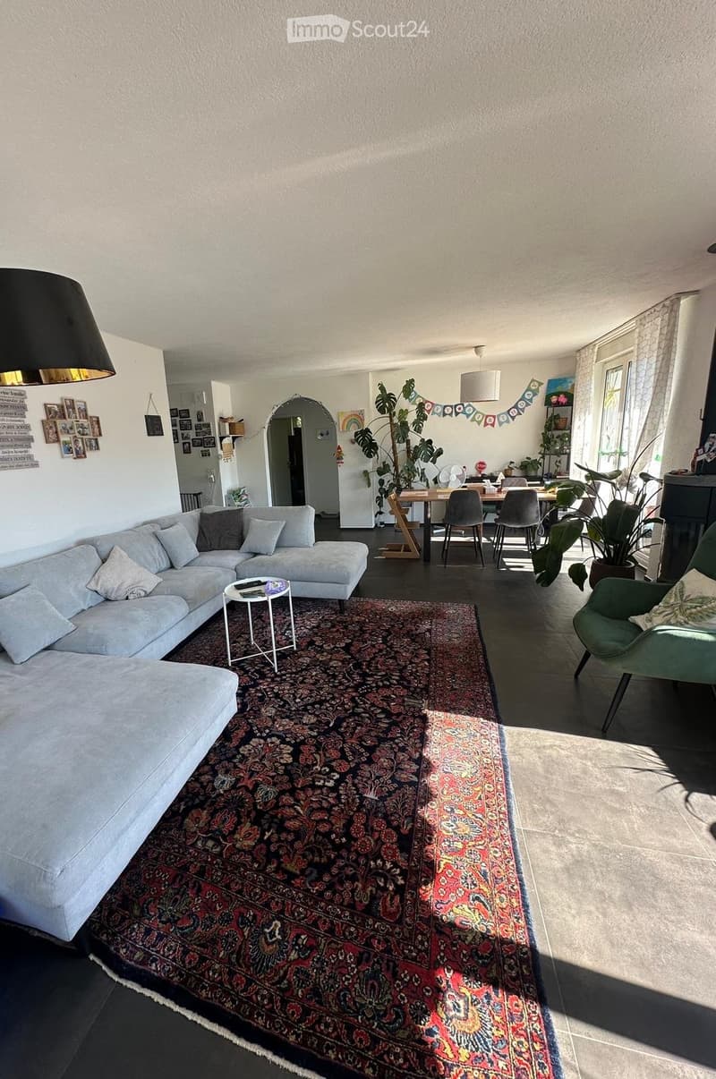 Living room with a grey sectional sofa, coffee table, green armchair, dining table with chairs, and large area rug.