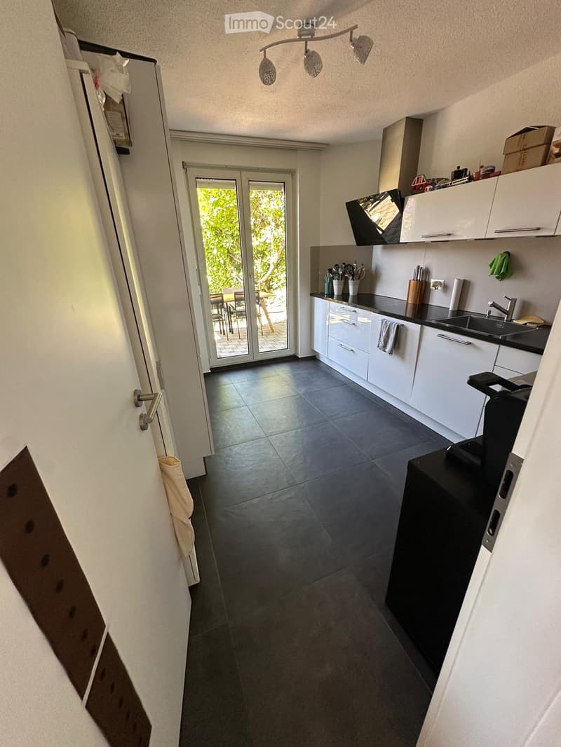 Modern kitchen with white cabinets, dark countertops, and a black floor. Features a sink, faucet, and a kitchen island with a built-in fridge.
