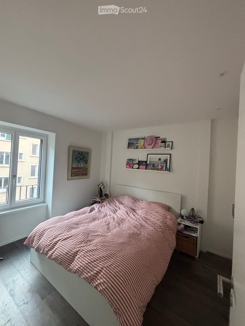 A furnished bedroom with a bed, nightstand, lamp, and shelves with picture frames and decorative items.