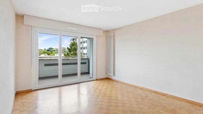 Empty room with wooden flooring, large sliding glass doors leading to a balcony, white walls, and a radiator on one wall.
