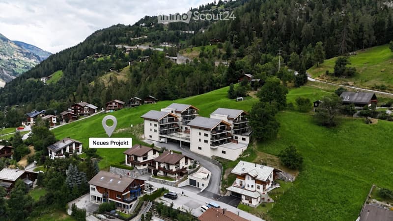 Aerial view of a residential area with multiple houses, surrounded by green hills and trees, with a central modern building highlighted.