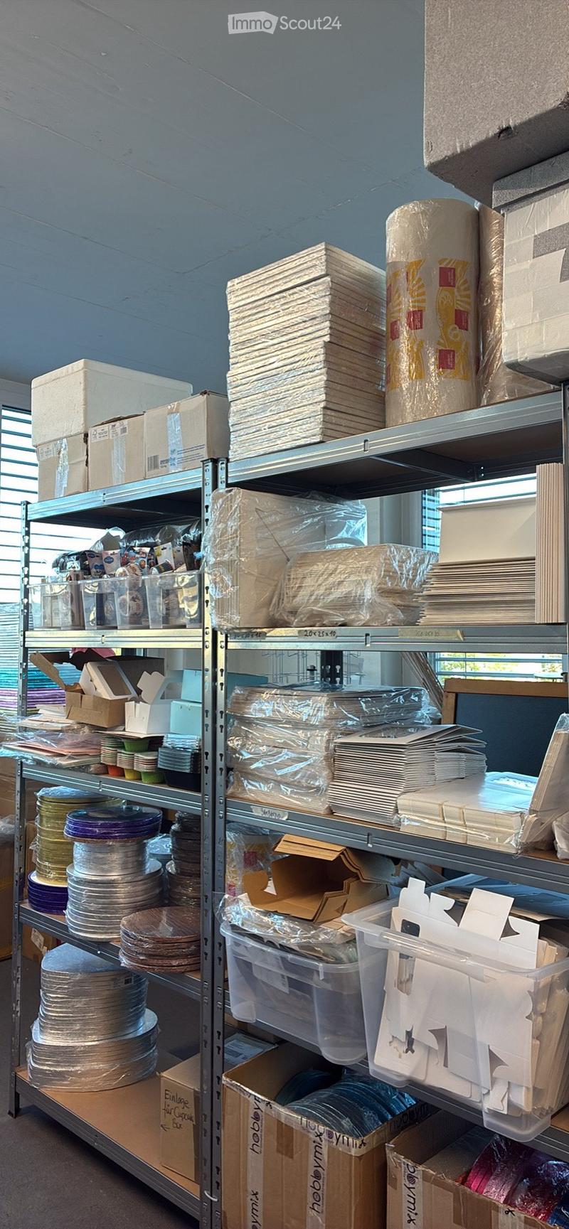 A storage room with metal shelving units filled with various items including boxes, plates, cups, and containers. The shelves are organized and the room has a practical, utilitarian design.