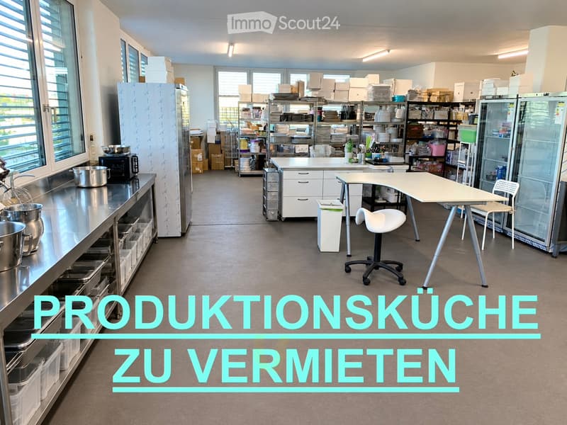 Production kitchen with stainless steel counters, refrigerator, microwave, tables, chairs, shelves, and storage bins.
