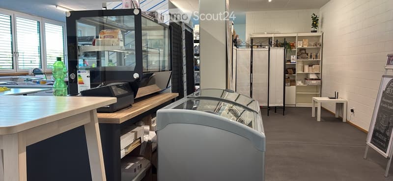 Modern retail or service area with a counter, cash register, refrigerator, shelves, and a small seating area.