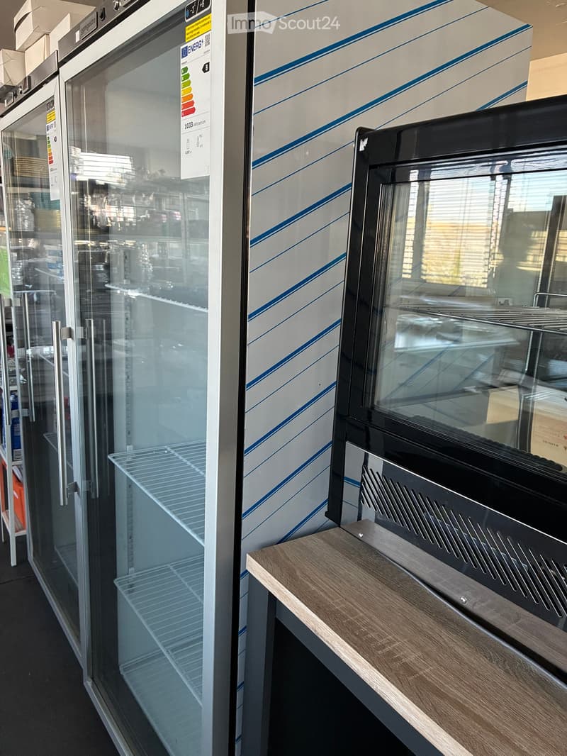 Modern kitchen display with a stainless steel refrigerator, microwave, and wooden shelf.