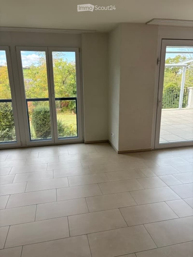 Empty room with large windows and sliding glass doors leading to a balcony, tiled floor, and neutral-colored walls.
