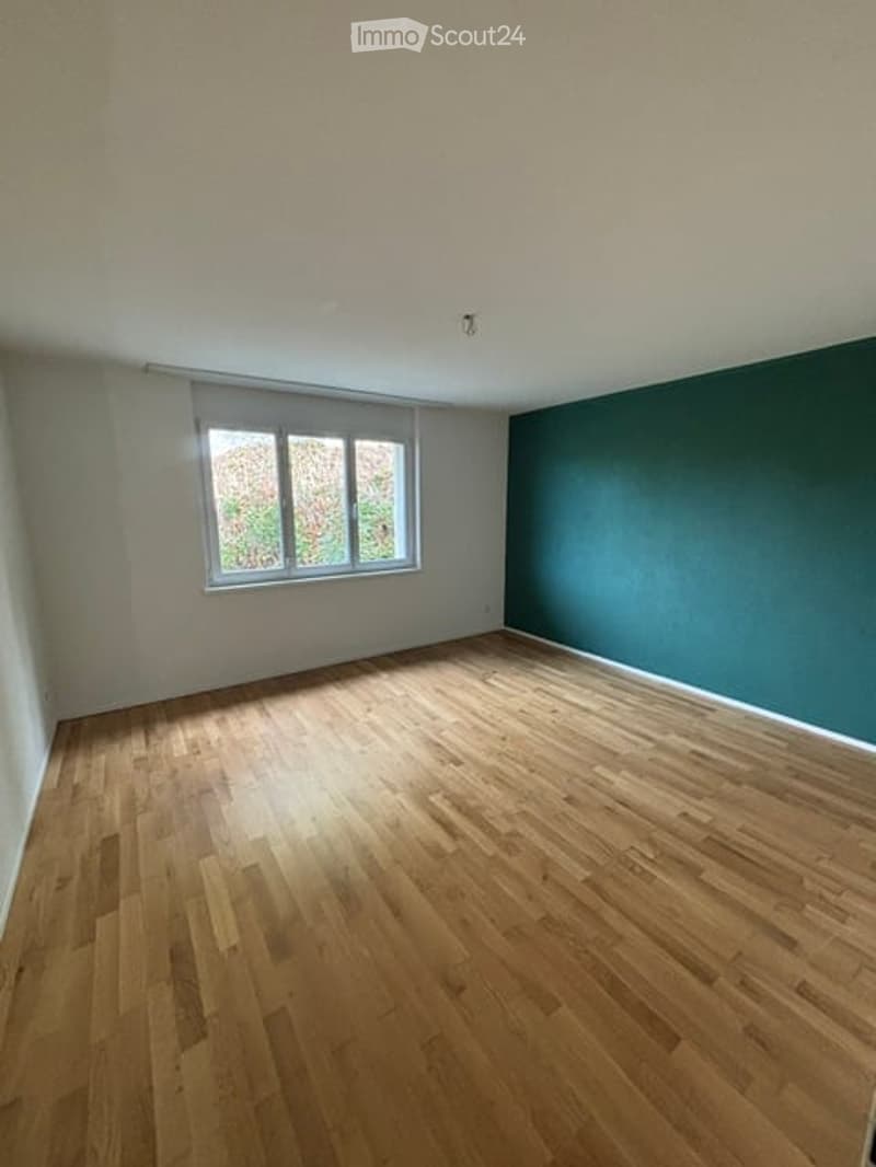 Completely empty room with wooden flooring, white walls, and a large window with blinds. No furniture or equipment present.