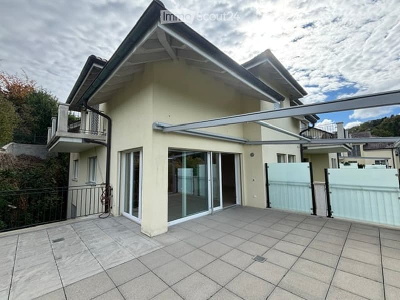 Modern two-story house with a balcony, large sliding glass doors, and a covered patio area.