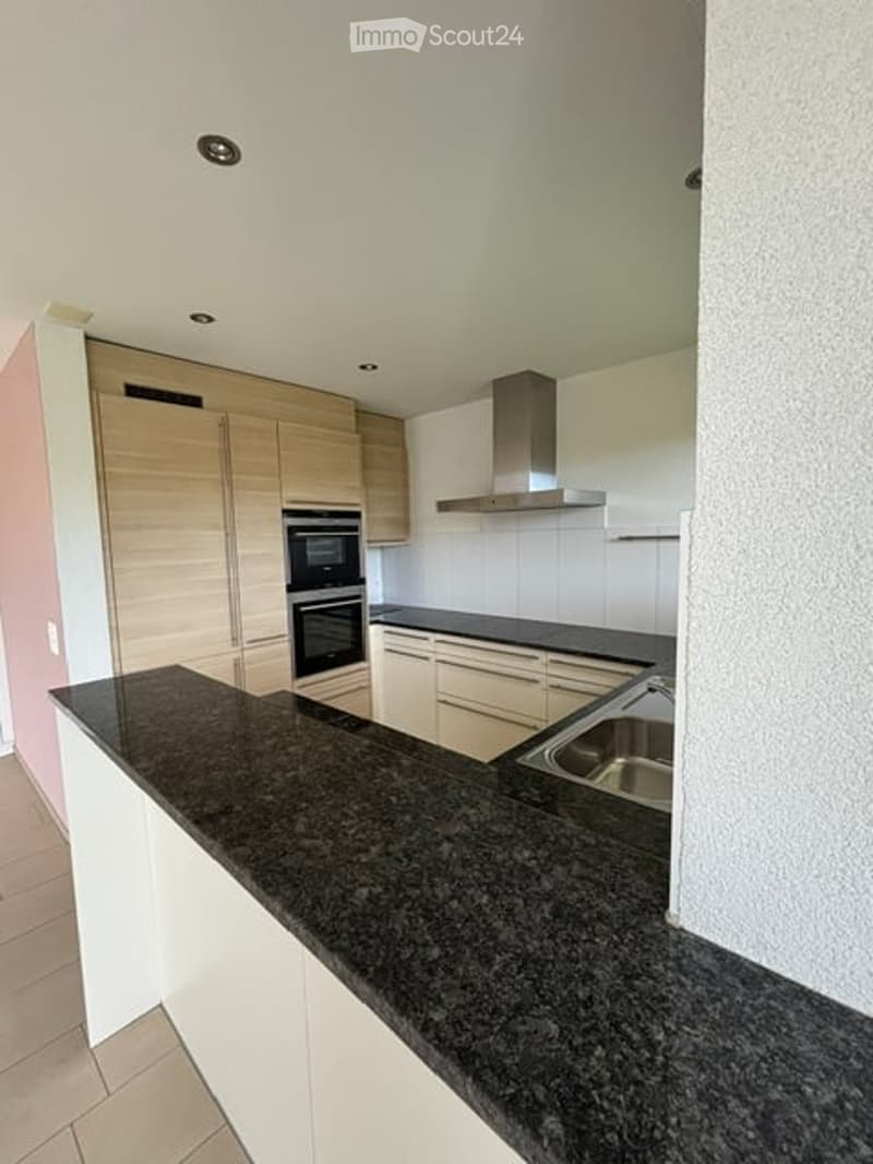 Modern kitchen with granite countertop, stainless steel sink, built-in oven, white cabinets, and a stainless steel range hood.