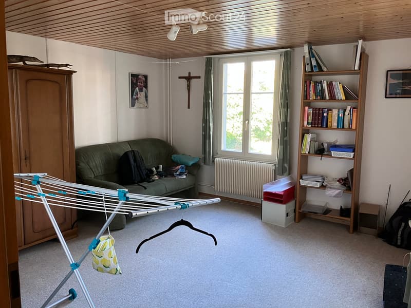 A cozy living room with a green sofa, a wooden bookcase filled with books, a wardrobe, a radiator, a picture frame, a cross, and a laundry rack with a handbag hanging on it.