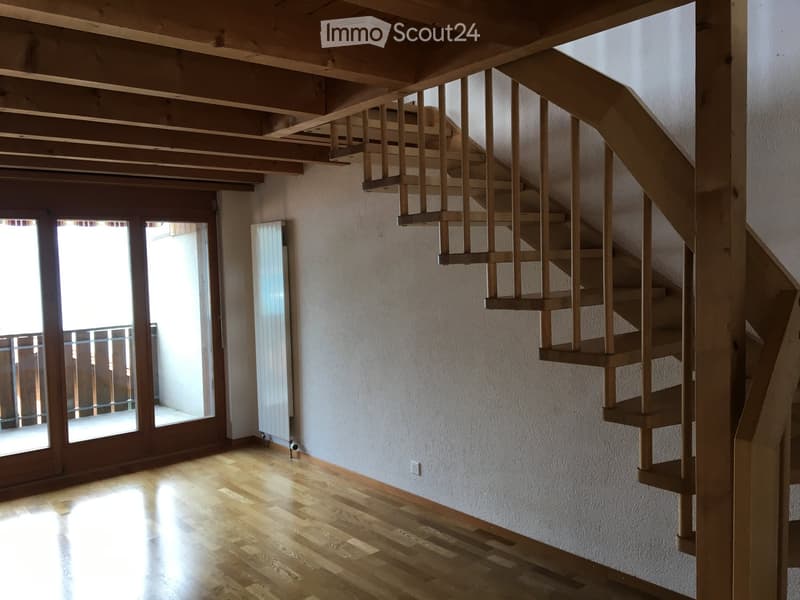 Spacious hallway with wooden flooring, white walls, and a wooden staircase leading to an upper level. Features large glass doors leading to an outdoor area.