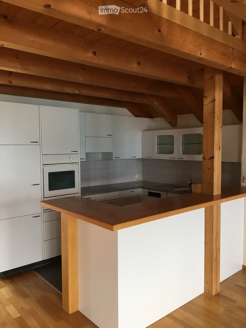 Modern kitchen with white cabinets, stainless steel appliances, wooden island, and exposed wooden beams on the ceiling.