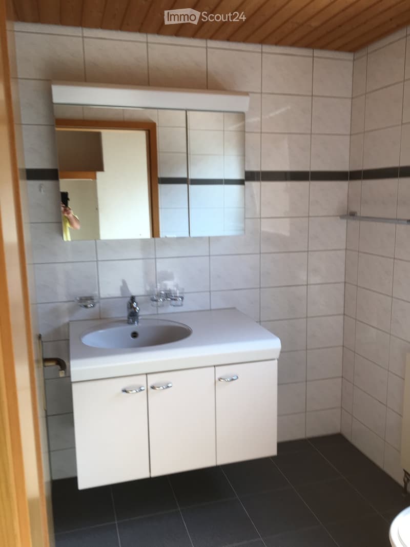Modern bathroom with white tiled walls, a white sink with a mirror above it, and a white cabinet with silver handles.