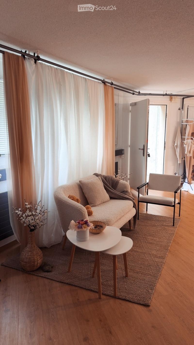 Modern living room with wooden flooring, a grey sofa, a white coffee table, a wicker vase, and a small chair.
