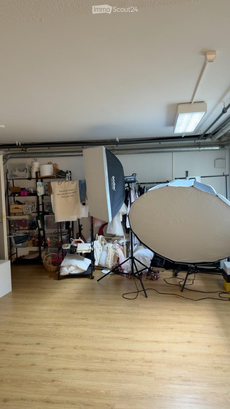 A room with wooden flooring, shelves filled with various items, a large umbrella light, a tripod, and a clothing rack with garments.