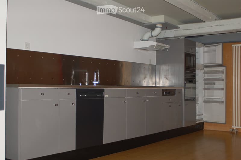 Modern kitchen with stainless steel appliances, grey cabinets, and a wooden floor.