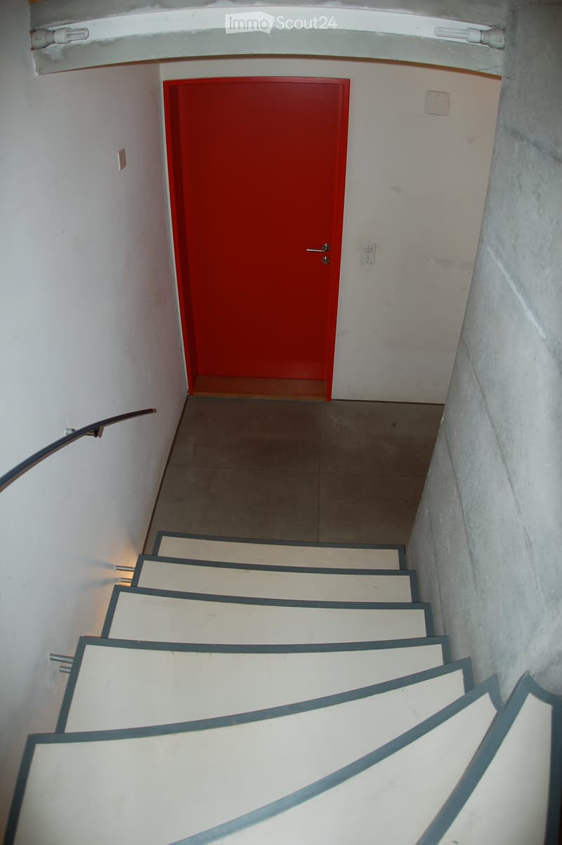 A narrow staircase with white steps and dark railings leads up to a red door at the top.