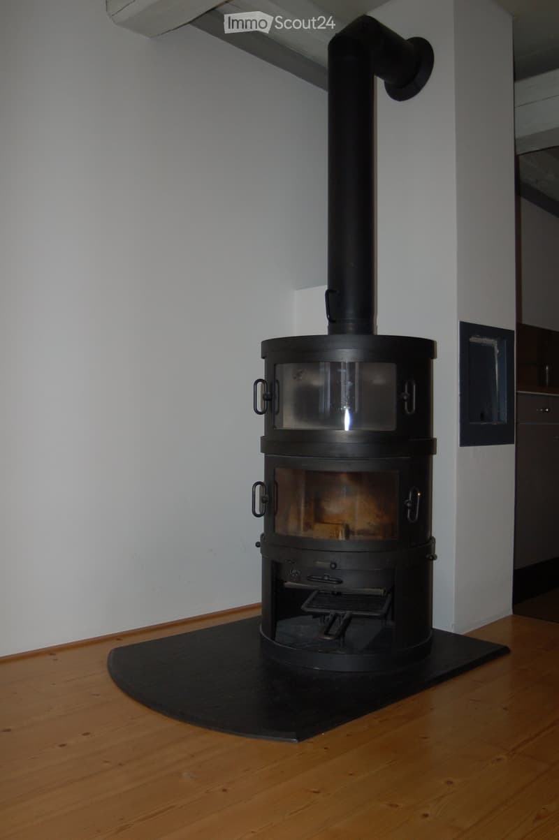 A modern black wood-burning stove with a glass door, situated on a wooden floor with a protective mat.