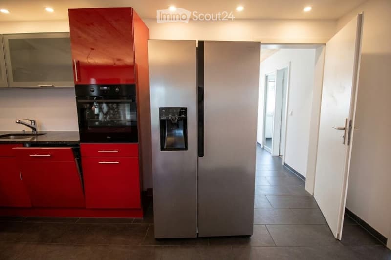 Modern kitchen with red cabinets, stainless steel appliances, and a large refrigerator. Features include a sink with a faucet, an oven, and built-in cabinets.