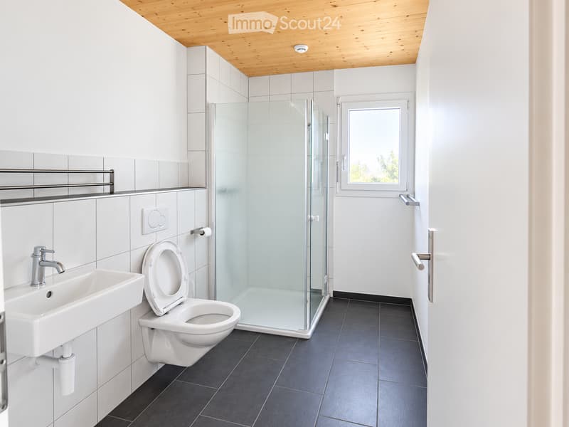 Modern bathroom with white tiles, a toilet, a sink with a chrome faucet, a glass-enclosed shower stall, and a towel rack.