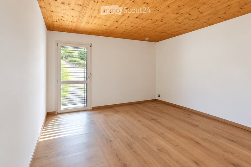 Empty room with light wooden flooring, white walls, and a sliding glass door leading outside.