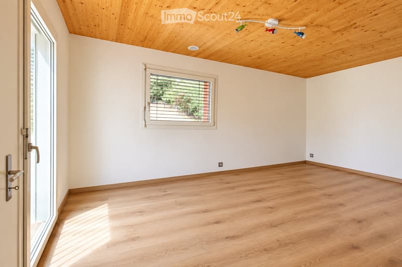 Empty room with light wooden flooring, white walls, and a wooden slatted ceiling. Features a large window with blinds and a glass door leading outside.