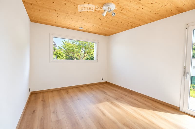 Empty room with light wooden flooring, white walls, and a wooden ceiling. Features a large window and a sliding glass door leading outside.