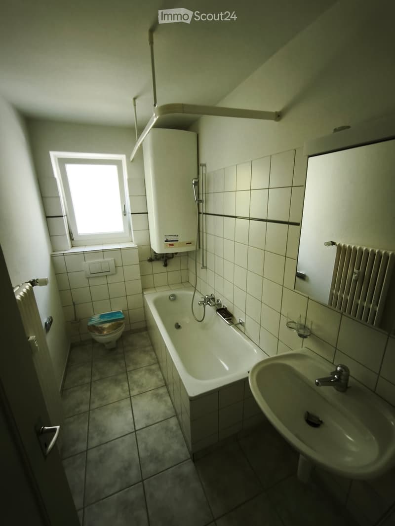 Bathroom with a bathtub, toilet, sink, and a window providing natural light. Includes a radiator and a shower hose attached to the wall.