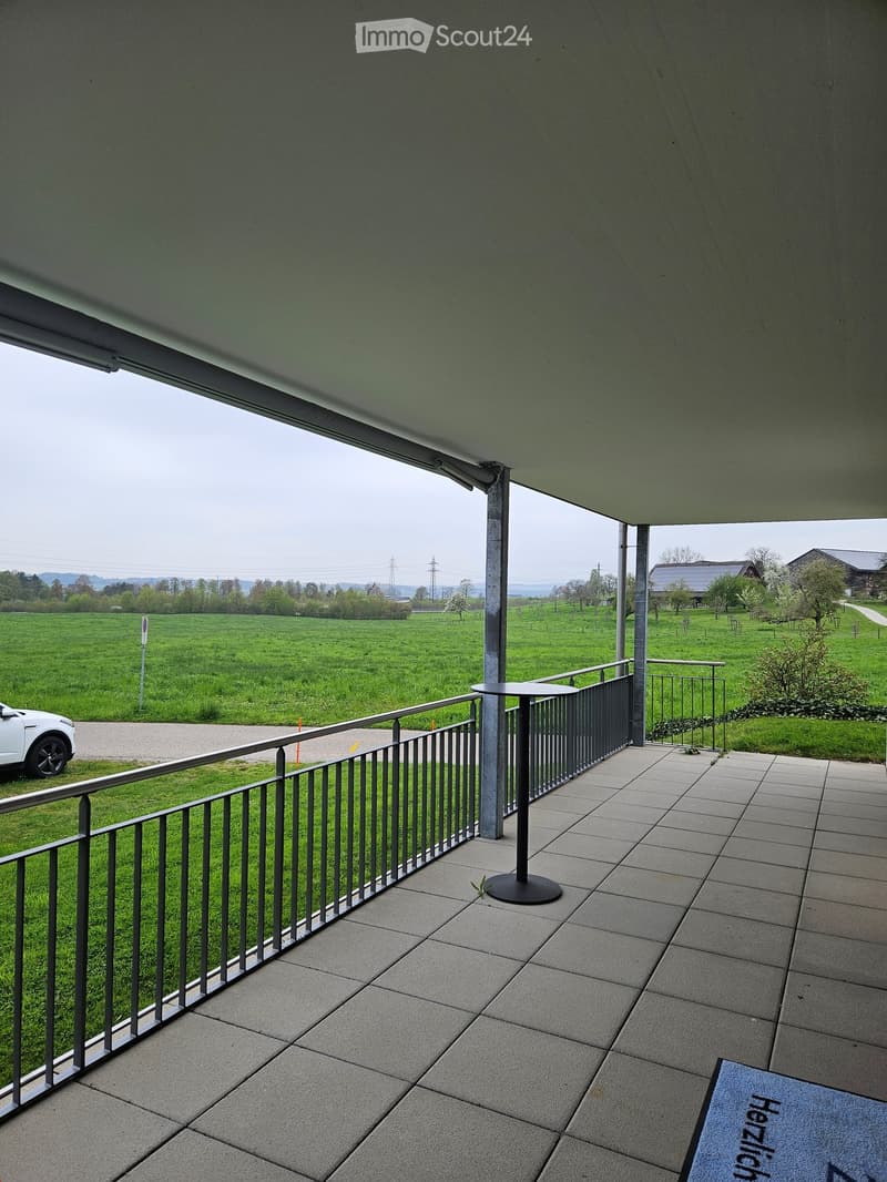Modern balcony with railings and tiled flooring, surrounded by grass and overlooking a large green field