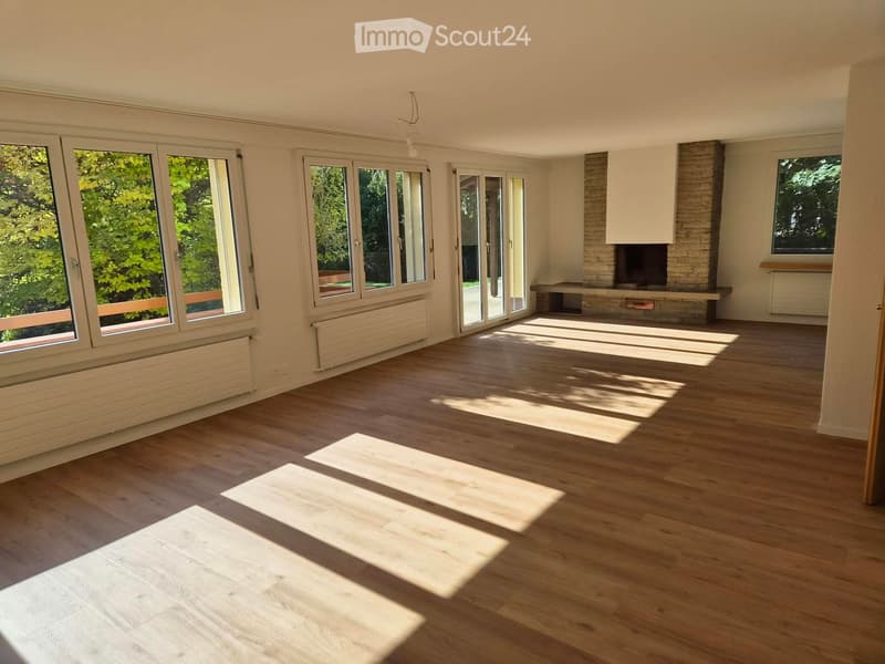 Empty room with wooden flooring, large windows, and a fireplace area.