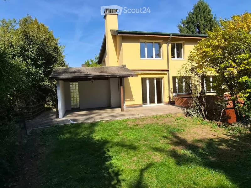 Two-story yellow house with a chimney, garage, and well-maintained garden.