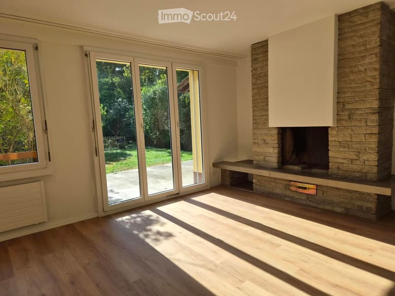 Bright living room with wooden flooring, large sliding glass doors leading to a garden, and a stone fireplace.