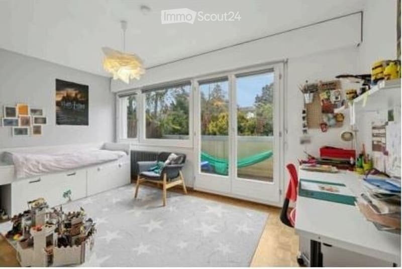 Bright, multi-functional room with large windows and sliding glass doors leading to a patio. Features a daybed, sofa, desk, and various decorative items.